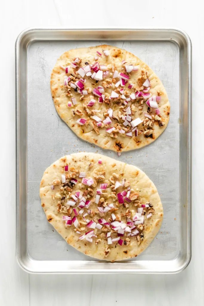 Top down view of naan bread topped with walnuts, garlic, and onion.