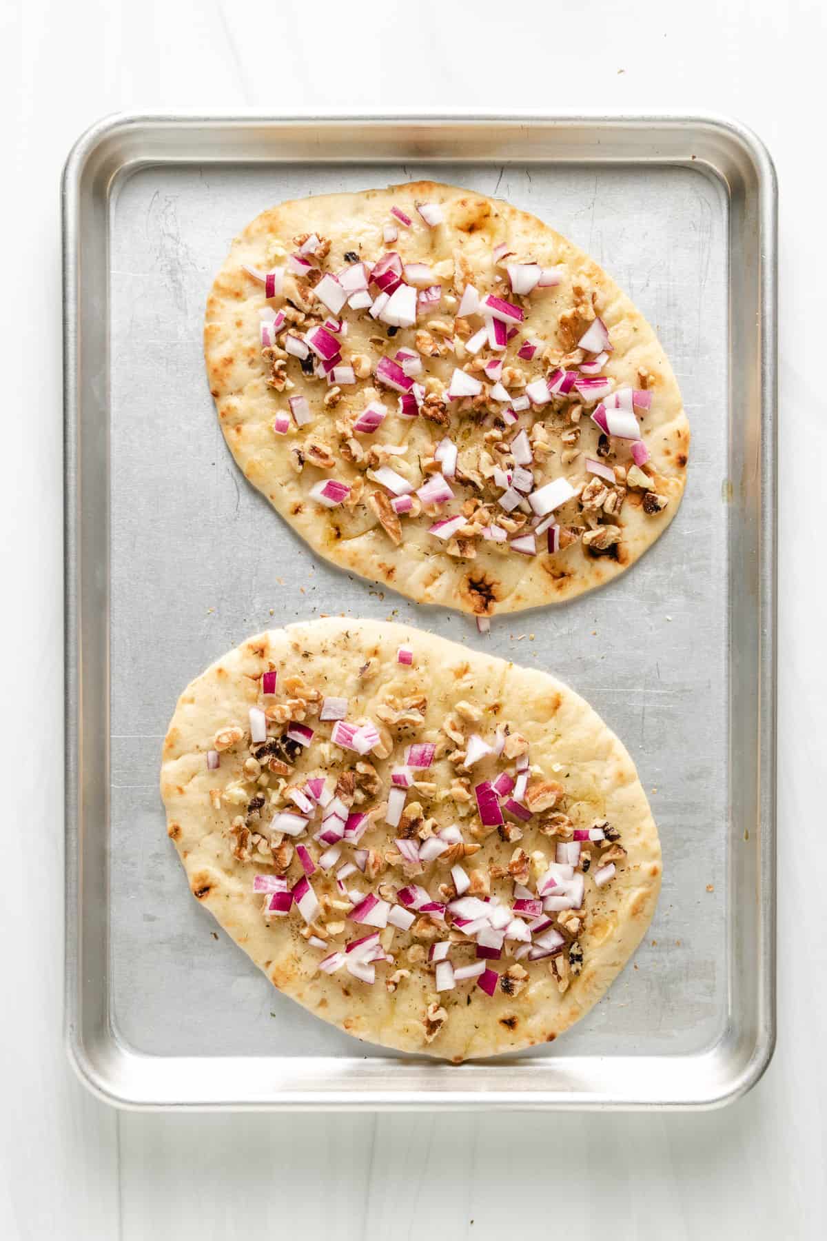 Top down view of naan bread topped with walnuts, garlic, and onion.