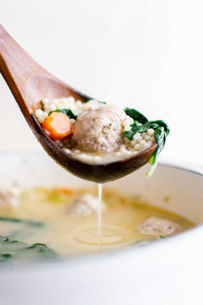 Italian wedding soup on a wooden ladle.