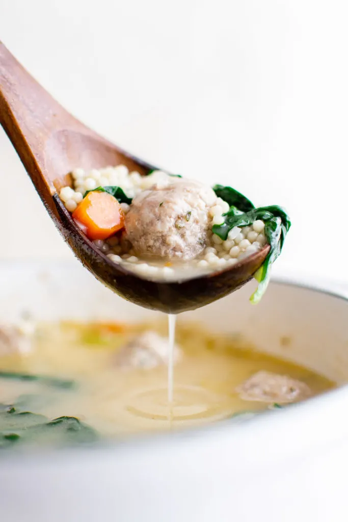 Italian wedding soup on a wooden ladle.
