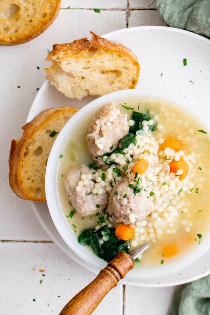 White bowl filled with soup, meatballs, and sliced bread.