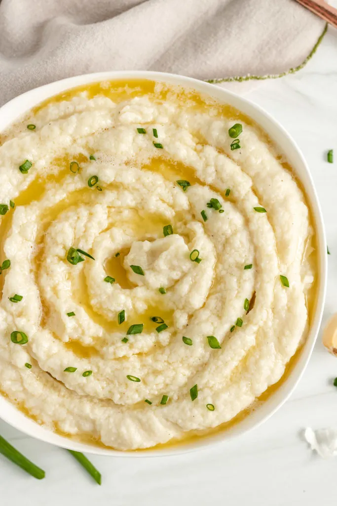 Top down view of mashed cauliflower with butter and green onions.