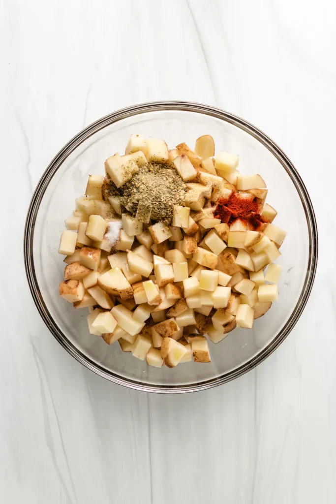 Top down view of potatoes and seasoning in a bowl.