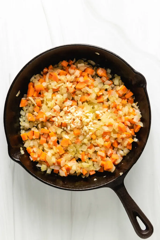 Top down view of carrots, onions, and garlic in cast iron.