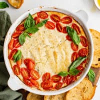 Top down view of baked goat cheese with cherry tomatoes and basil.