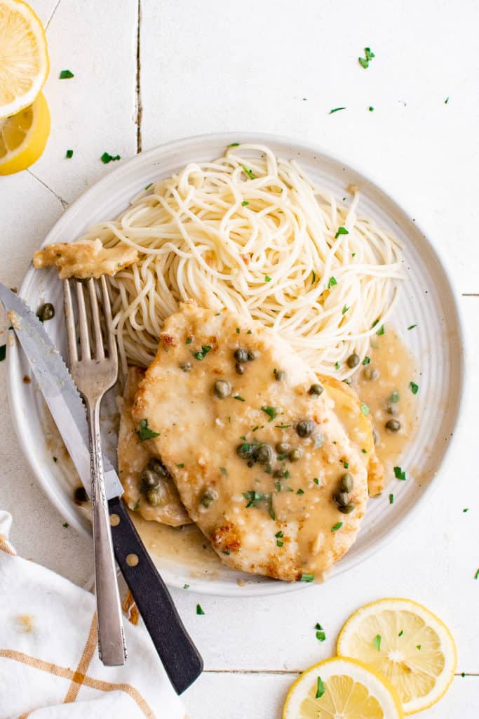 Top down view of chicken piccata with pasta on a plate.