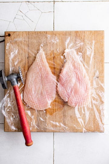 Chicken breast and mallet on a cutting board.