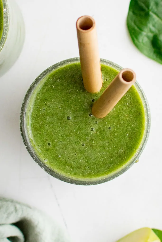 Top down view of a green smoothie in a glass with two straws.