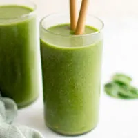 Glass filled with a green smoothie and straws.