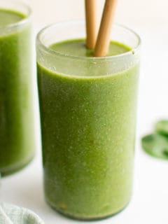 Glass filled with a green smoothie and straws.