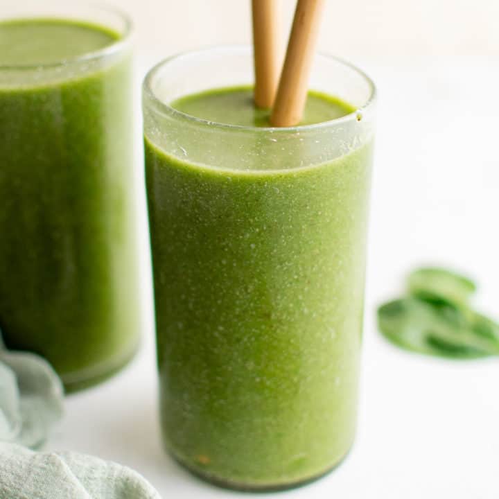 Glass filled with a green smoothie and straws.