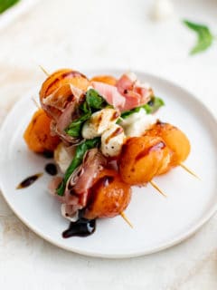 Balsamic drizzled prosciutto and melon on a plate.