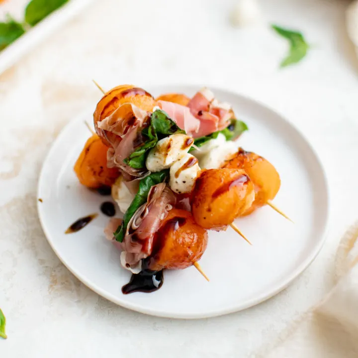 Balsamic drizzled prosciutto and melon on a plate.