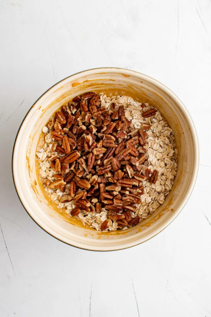 Chopped pecans on top of oatmeal batter in a mixing bowl.