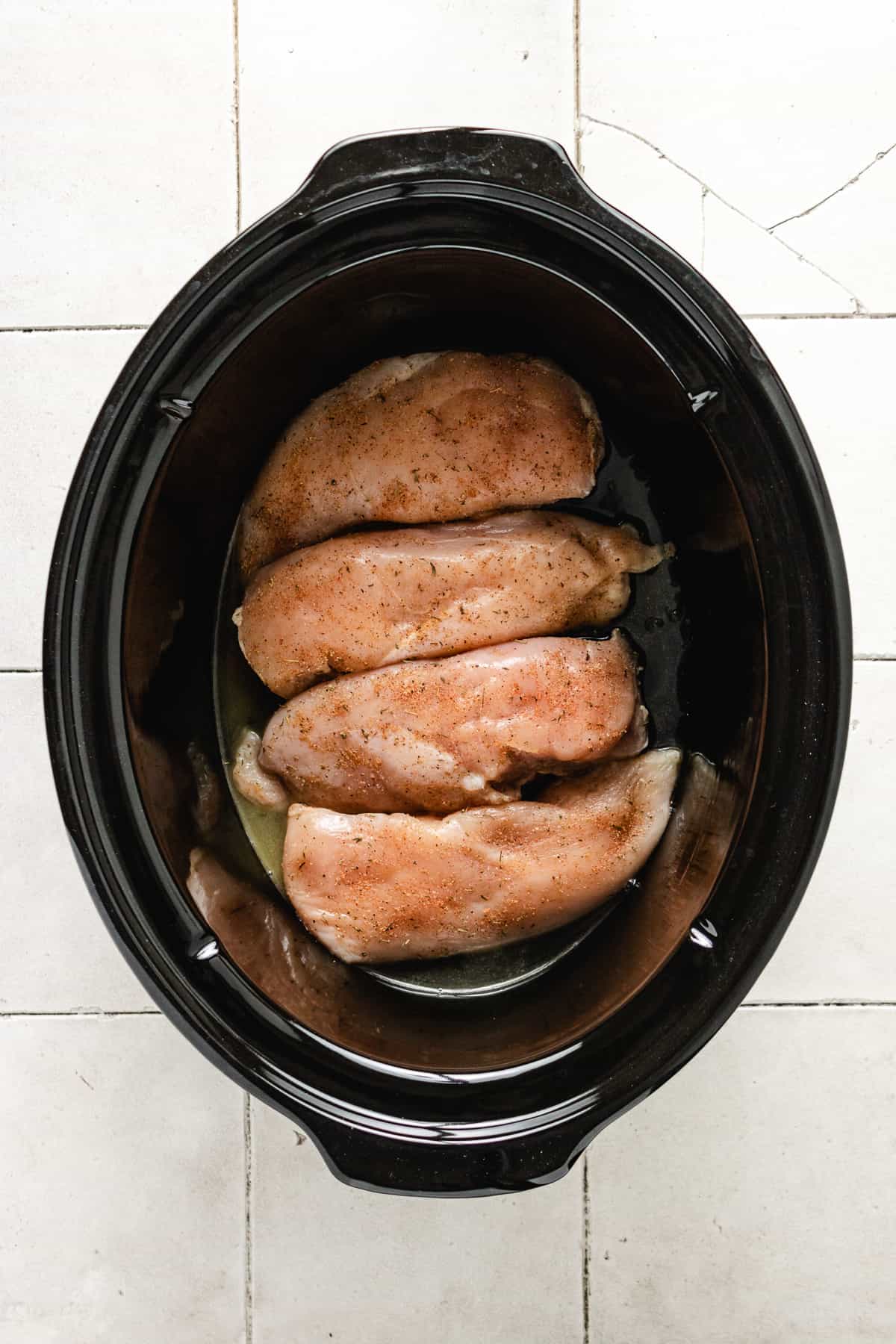 Top down view of raw chicken breasts in a slow cooker.