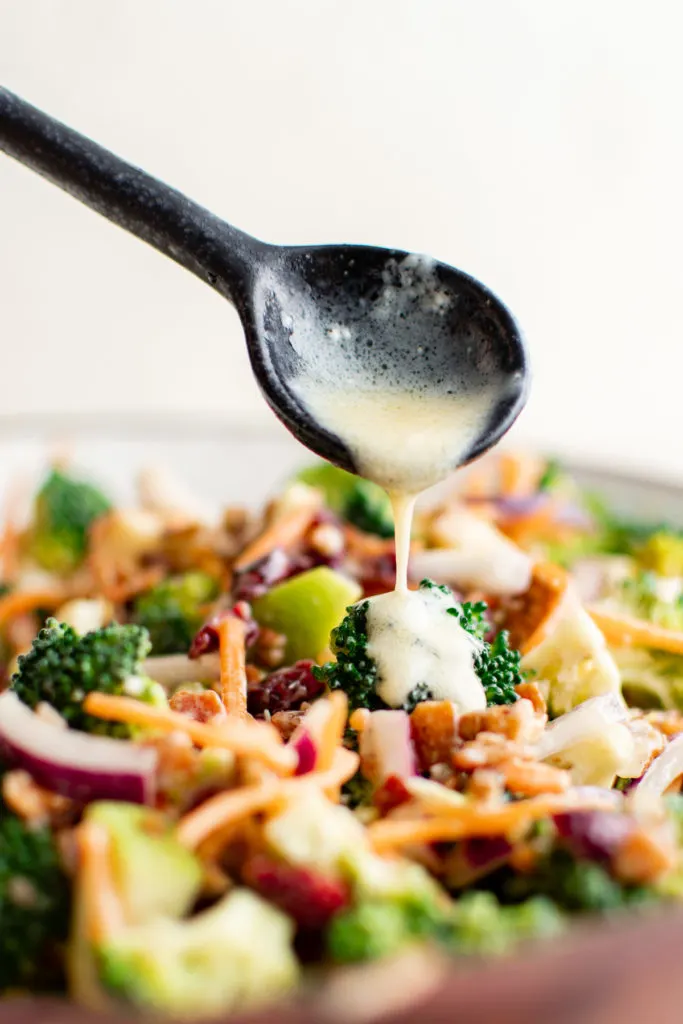 Dijon dressing being drizzled over broccoli bacon salad.