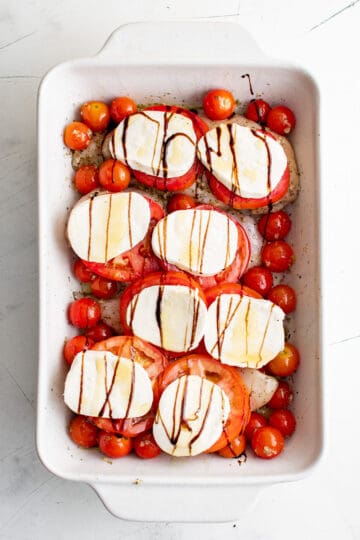 Slices of mozzarella cheese, balsamic glaze and tomatoes on top of chicken.