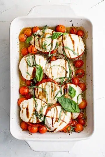 Baked chicken caprese in a white casserole dish.