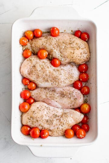 Seasoned chicken breasts laid on top of cherry tomatoes.