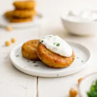 Two chickpea fritters on a plate with dipping sauce.