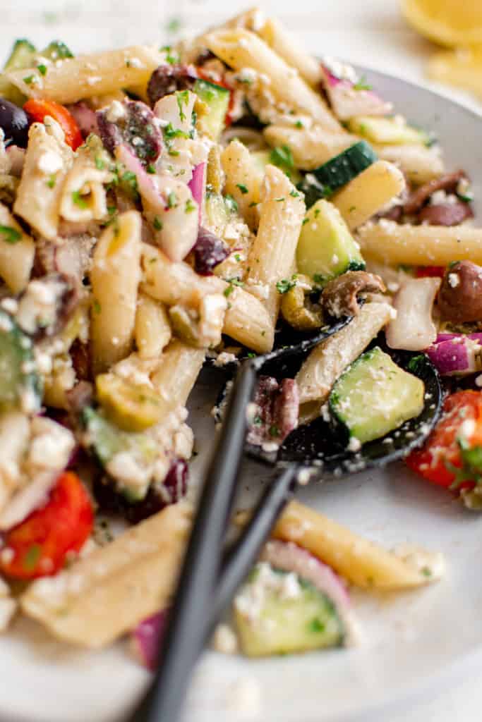 Close up view of tongs holding pasta salad.
