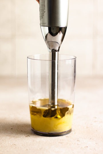 Immersion blender in a plastic cup in the process of making mayo.