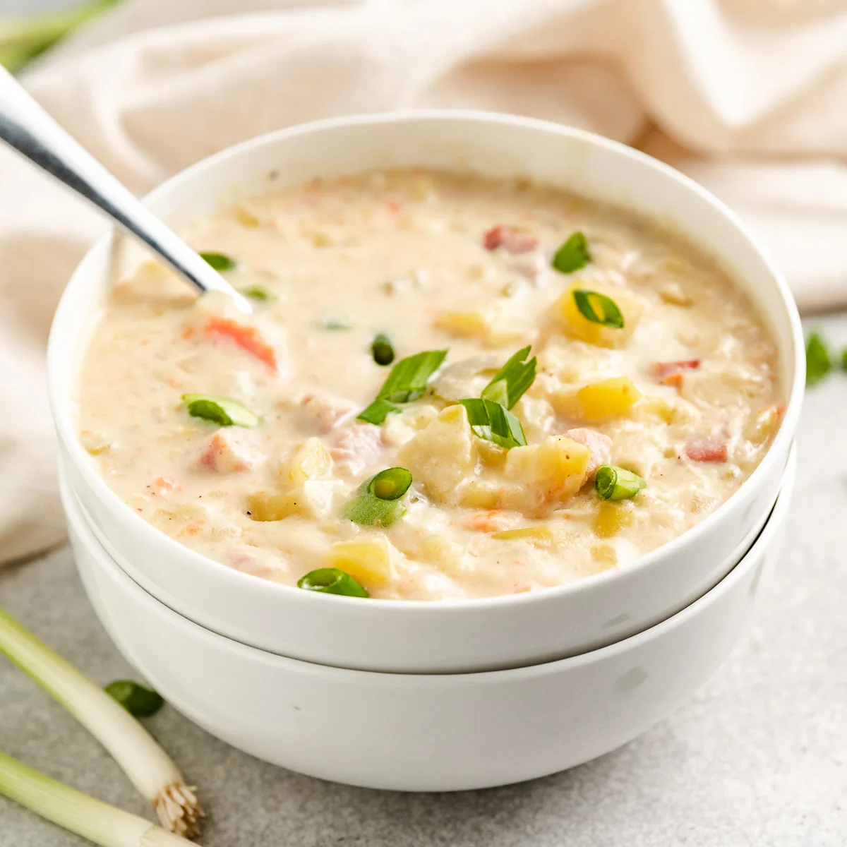 Spoon in a white bowl of crockpot ham and potato soup.