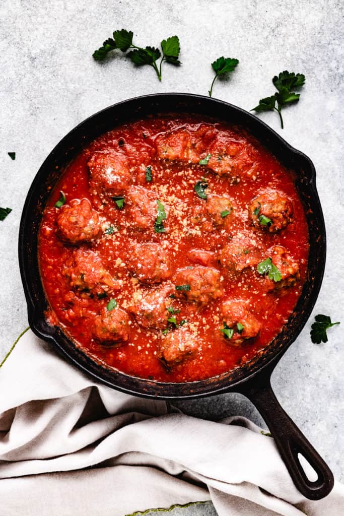 Cast iron skillet filled with marinara sauce and meatballs.