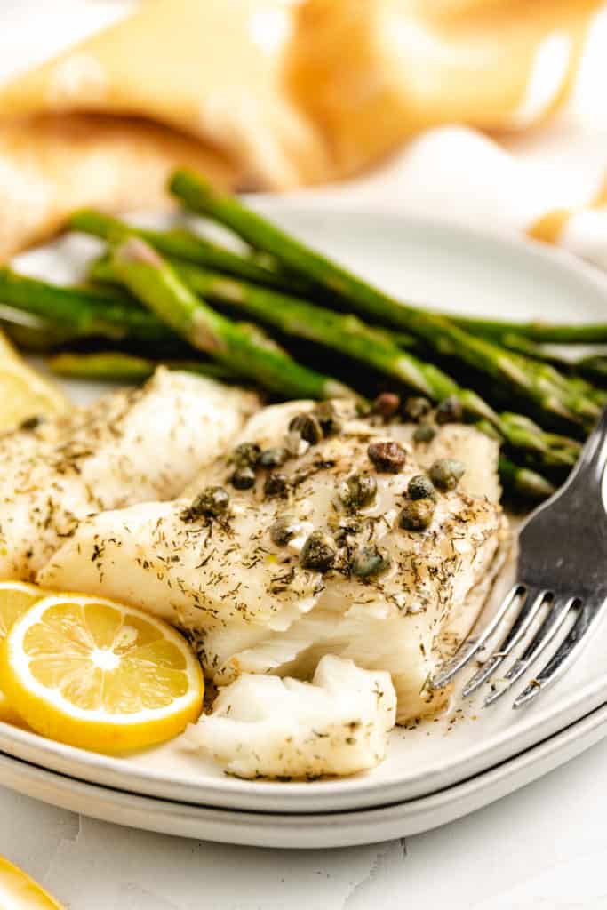 Fish with lemon and steamed veggies on a white plate.