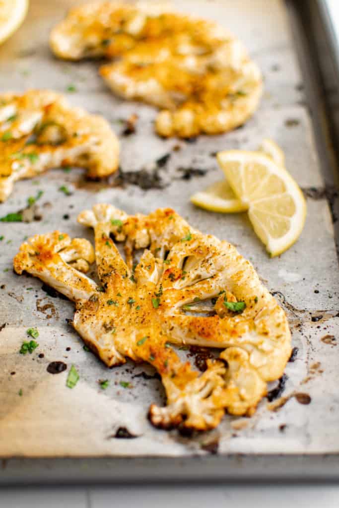 Side view of roasted cauliflower steaks and lemon on a pan.