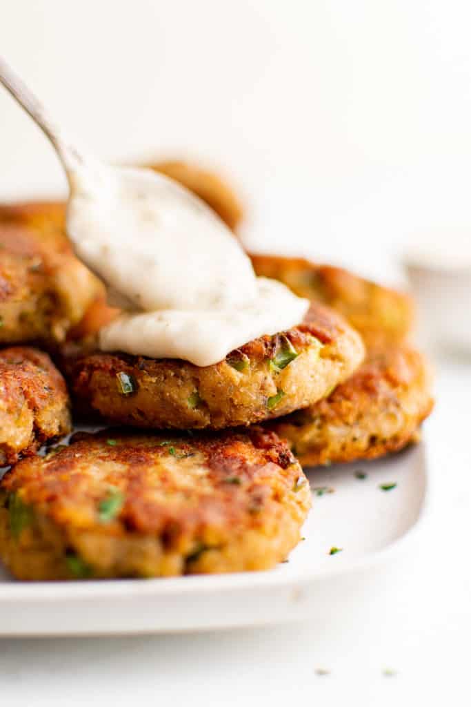 Tartar sauce being spooned onto a salmon cake.