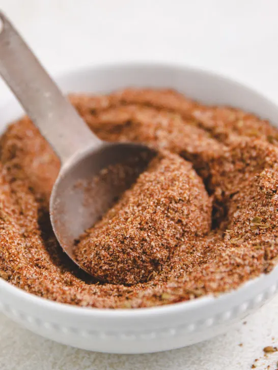 Metal spoon scooping taco seasoning out of a bowl.