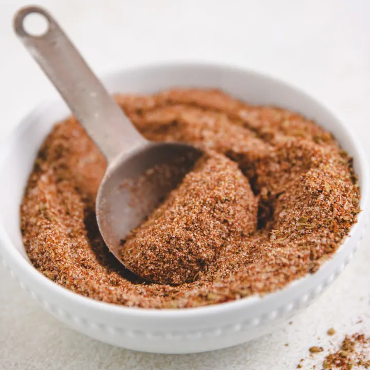 Metal spoon scooping taco seasoning out of a bowl.