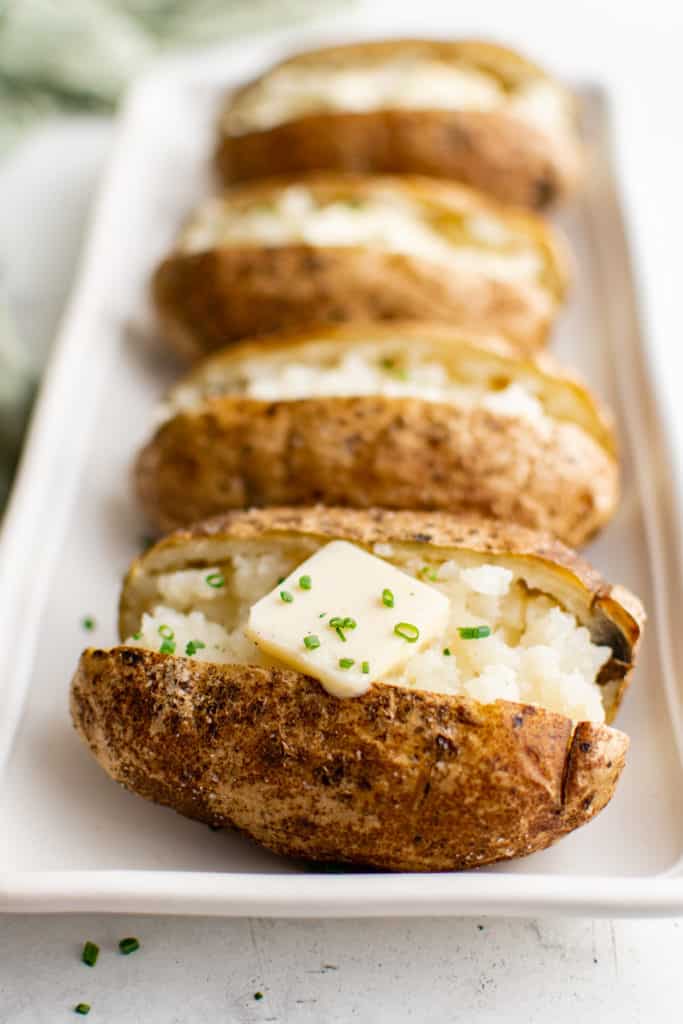 Several baked potatoes with butter and chives.