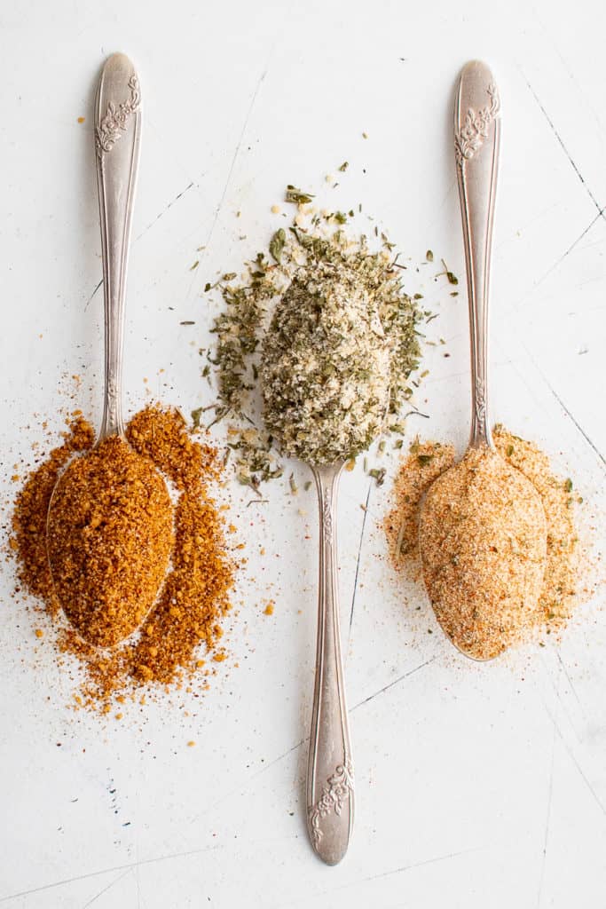 Top down view of three spoons full of seasoning blends.