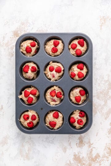 Unbaked muffins with raspberries in a pan.