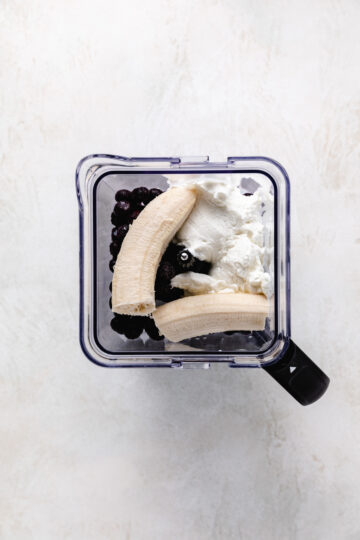 Bananas in a blender with yogurt and blueberries.