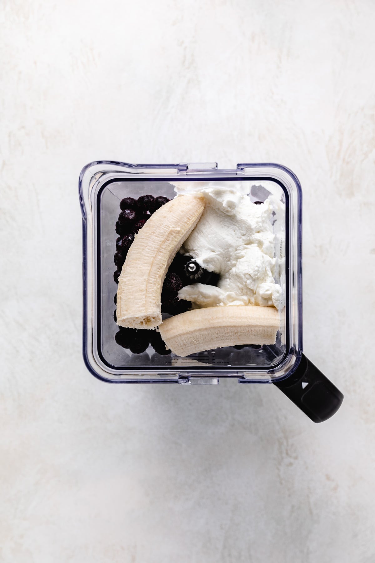 Bananas in a blender with yogurt and blueberries.