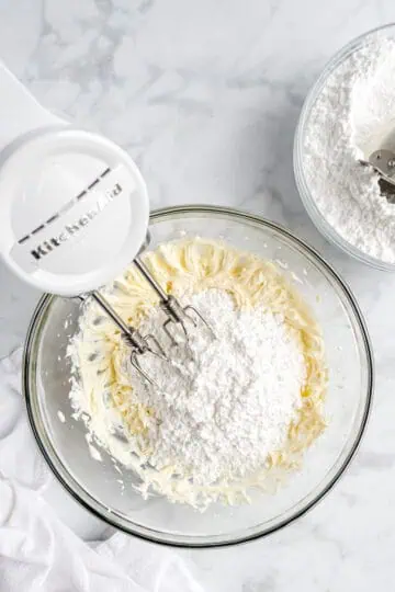 Powdered sugar added to a bowl of creamed sugar.