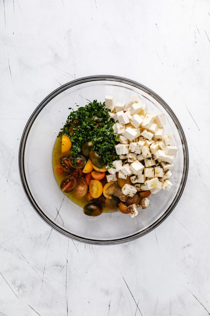 Tomatoes, bowls, herbs, and dressing in a bowl.