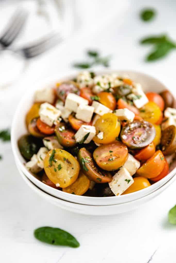 White bowls filled halved tomatoes, cheese and dressing.