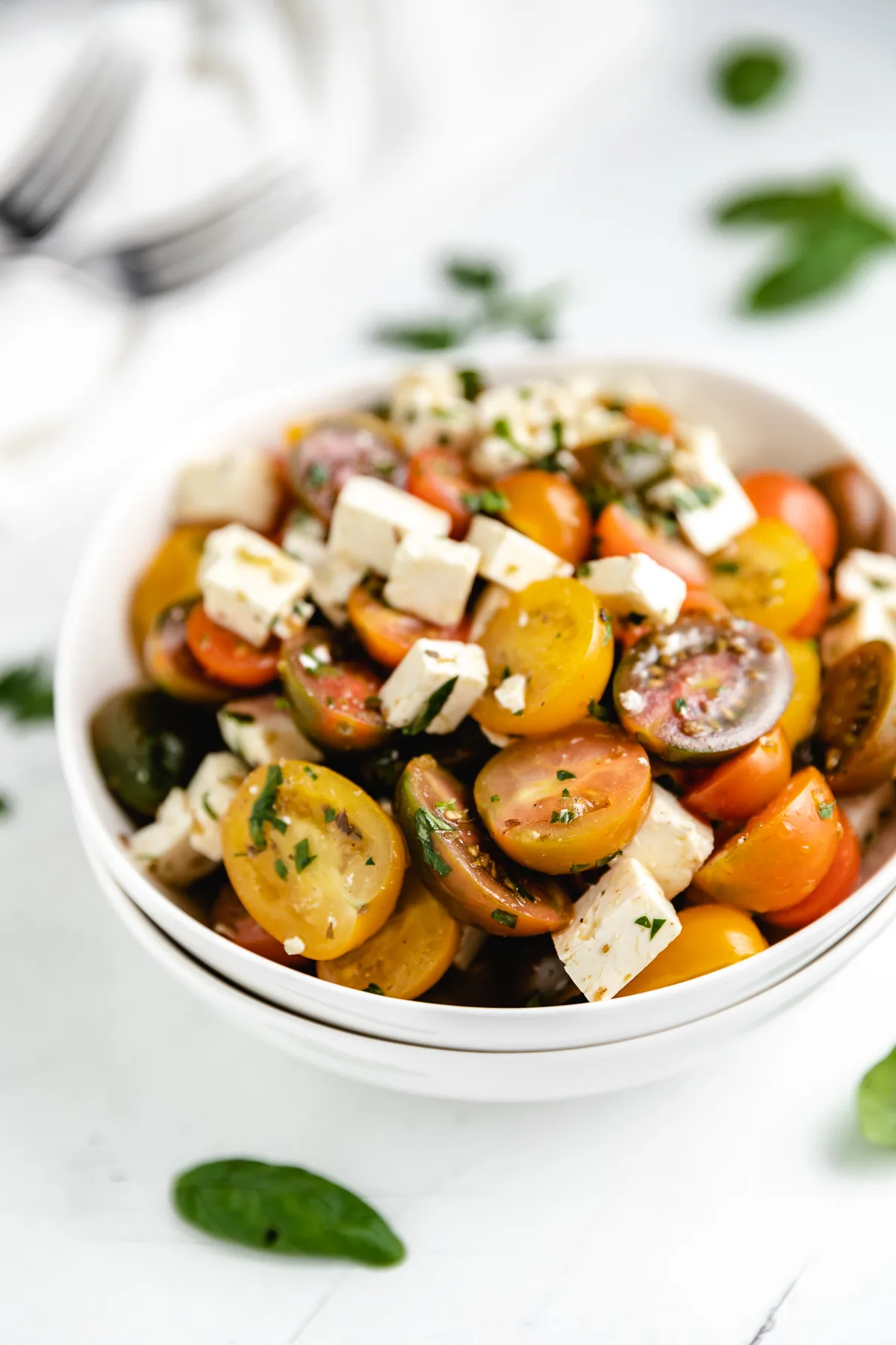 White bowls filled halved tomatoes, cheese and dressing.