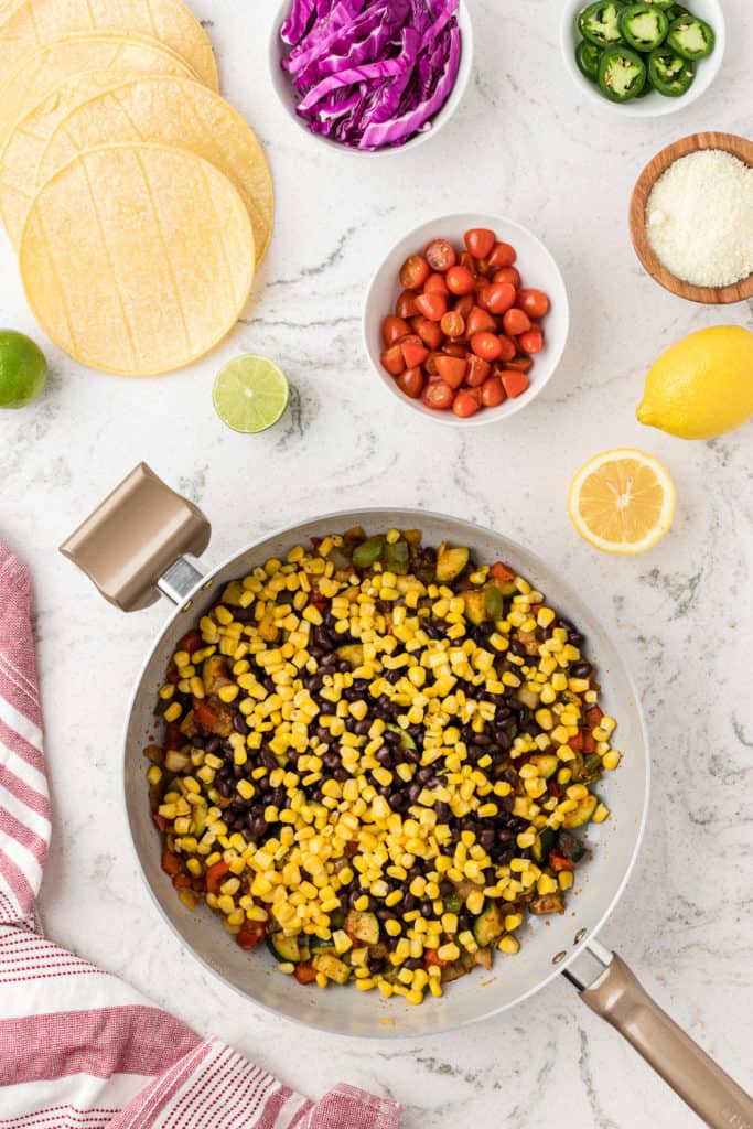 Corn and black beans added to a skillet of vegetables.