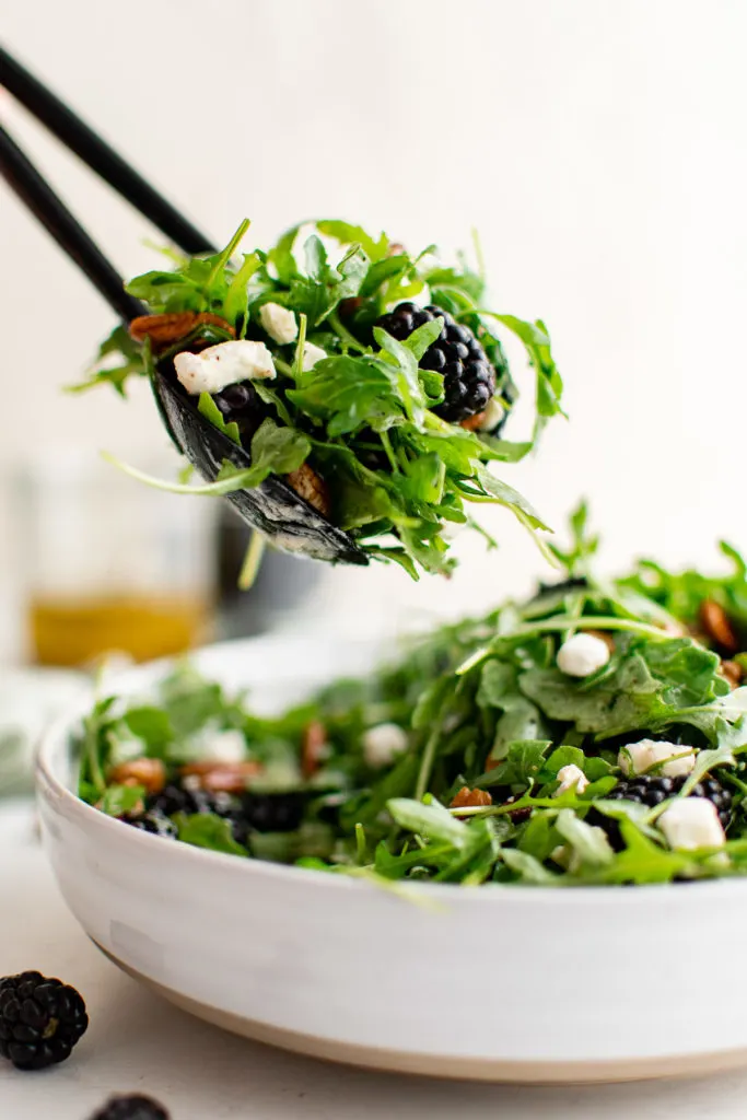 Tongs placing salad in a bowl.