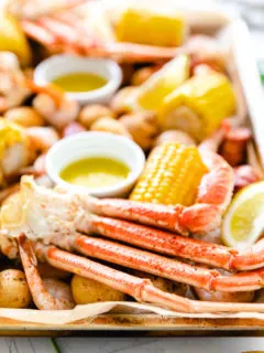 Side view of crab legs, corn, and potatoes on a baking sheet.