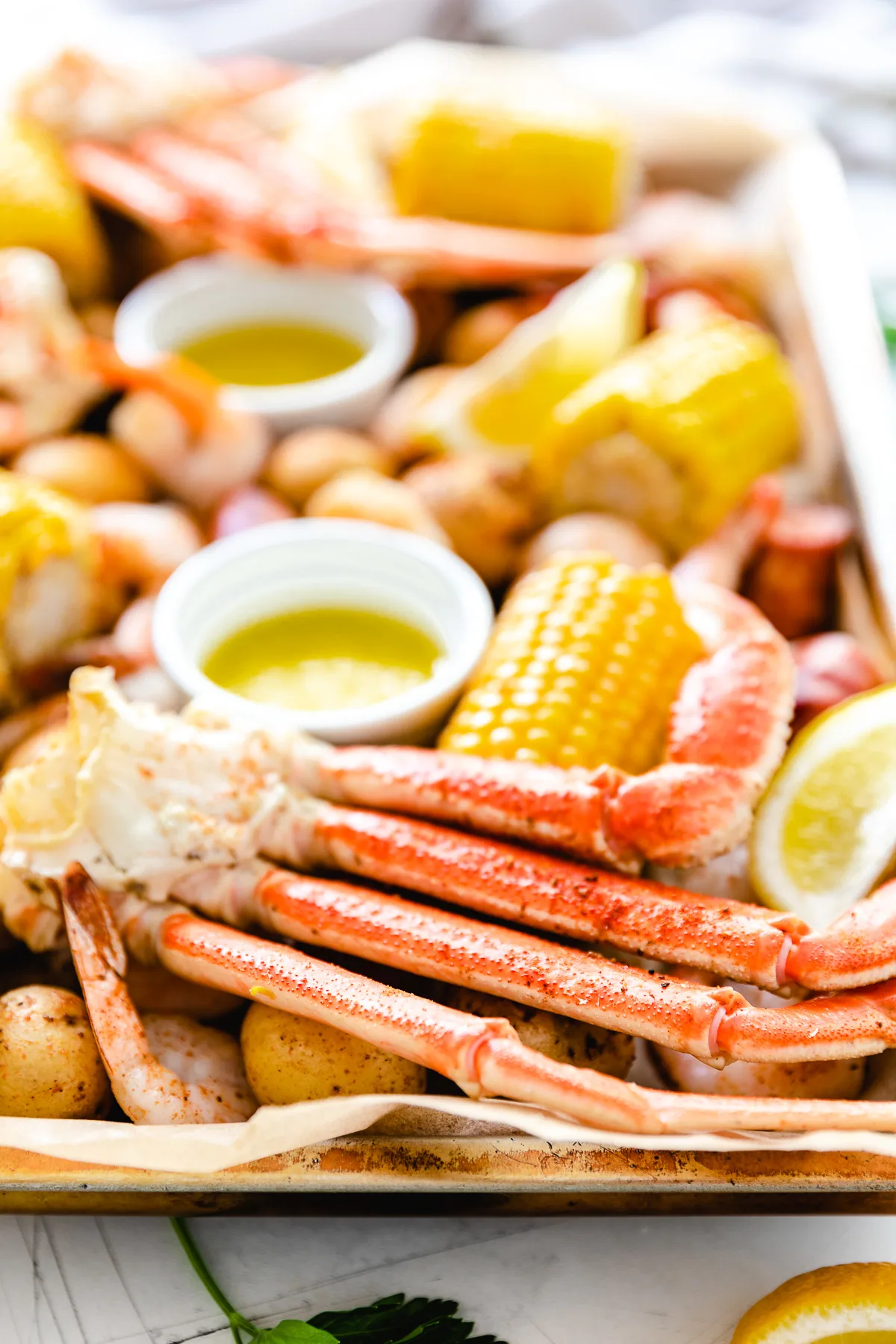 Side view of crab legs, corn, and potatoes on a baking sheet.