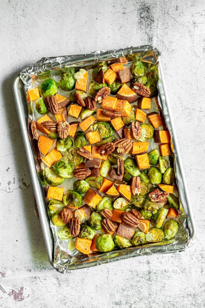 Pecans added to roasted vegetables on a baking sheet.