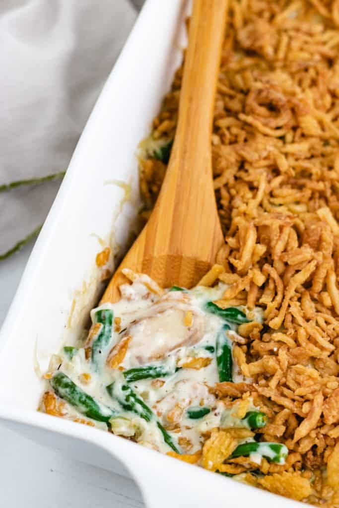 Wooden spoon scooping green bean casserole out of a baking dish.
