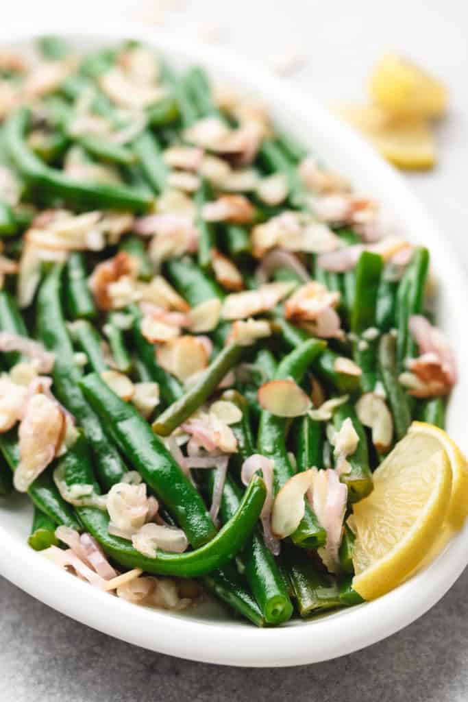 Close up view of green beans almondine on a white dish.