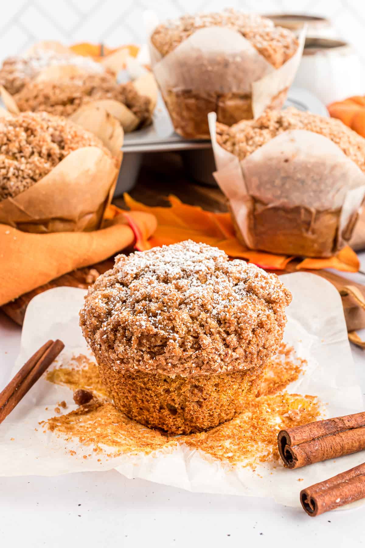 Pumpkin muffin sitting on open paper with cinnamon sticks.